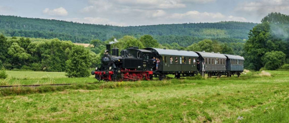 Dampfeisenbahn mir drei Waggons fährt durch grüne Landschaft