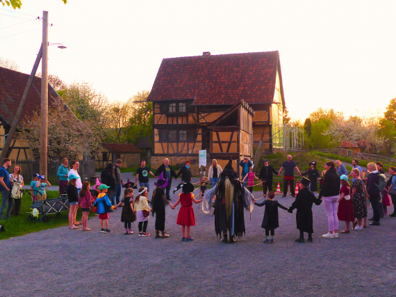 Kinder und Erwachsene stehen vor Fachwerkgebäude im Kreis und halten sich an den Händen