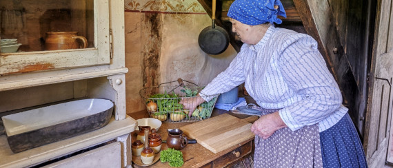 Frau in historischer Kleidung bereitet Essen in einer Küche zu