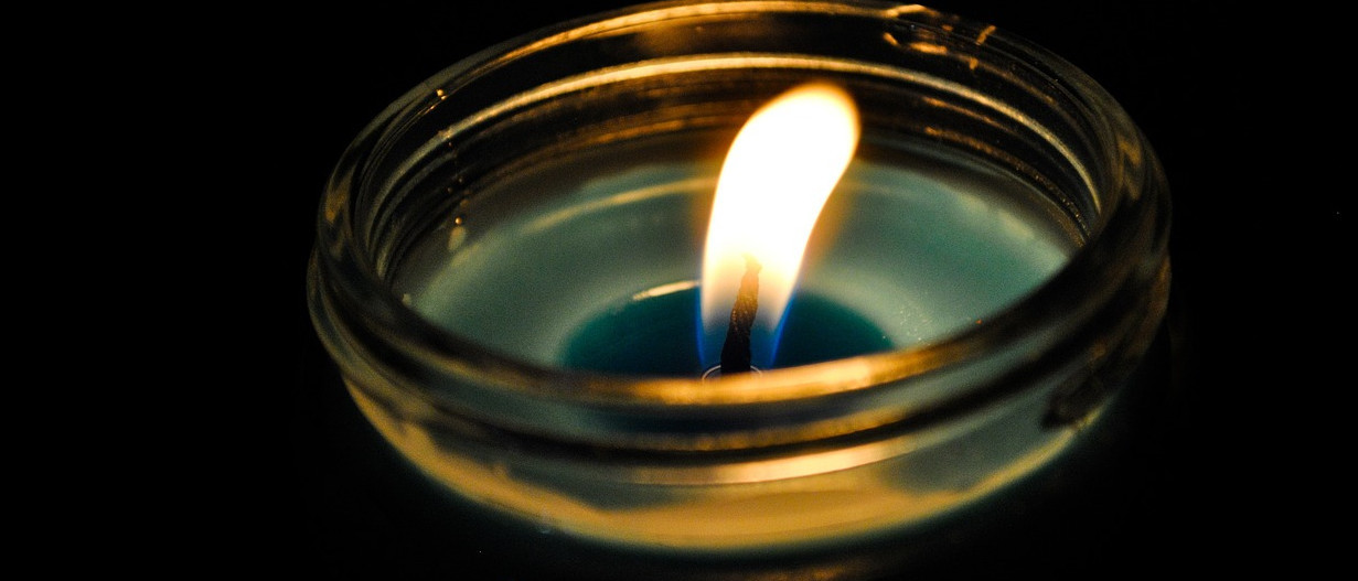 Brennende Kerze im Glas vor dunklem Hintergrund