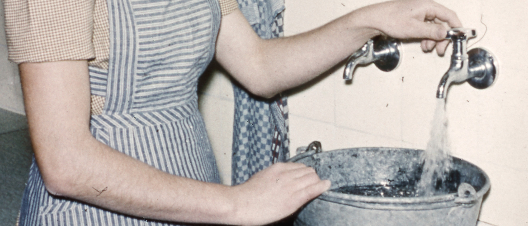 Frau befüllt Eimer am Wasserhahn