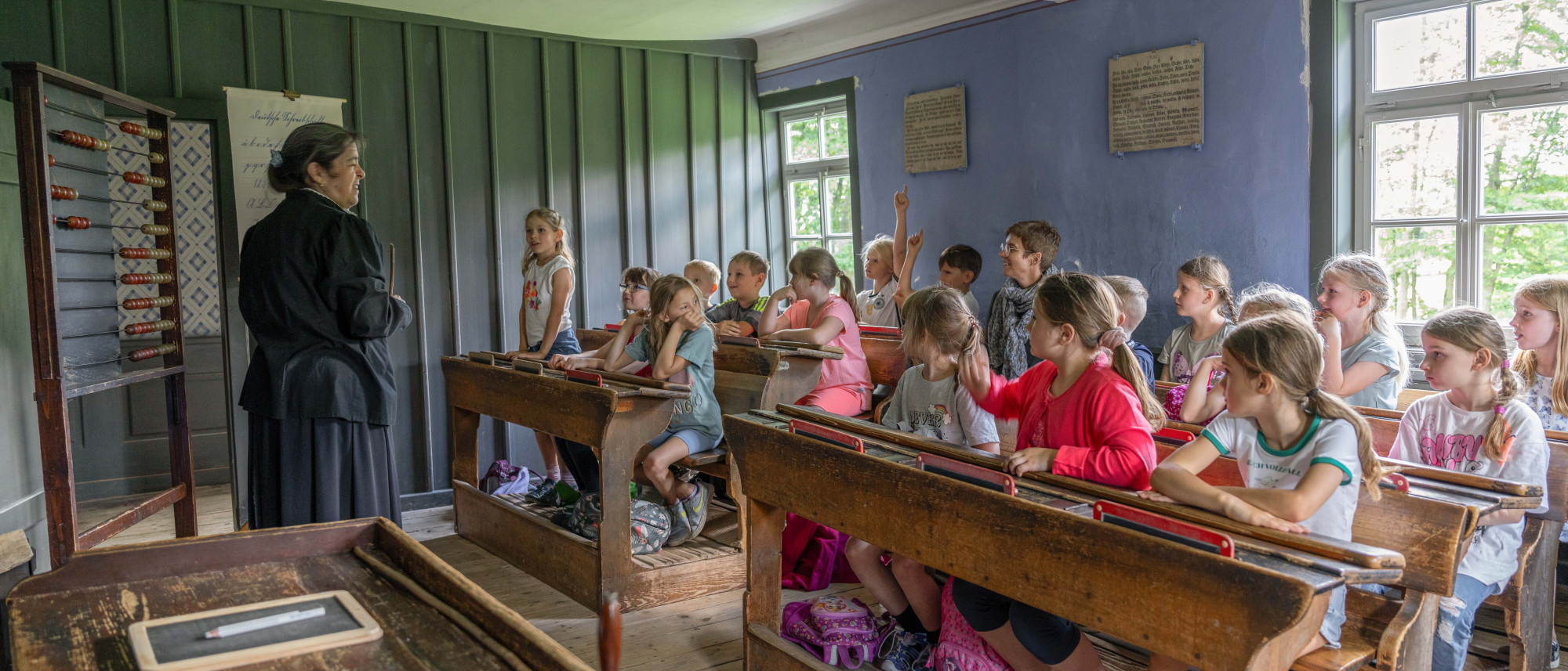 Lehrerin vor Schulklasse in historisch eingerichtetem Unterrichtsraum
