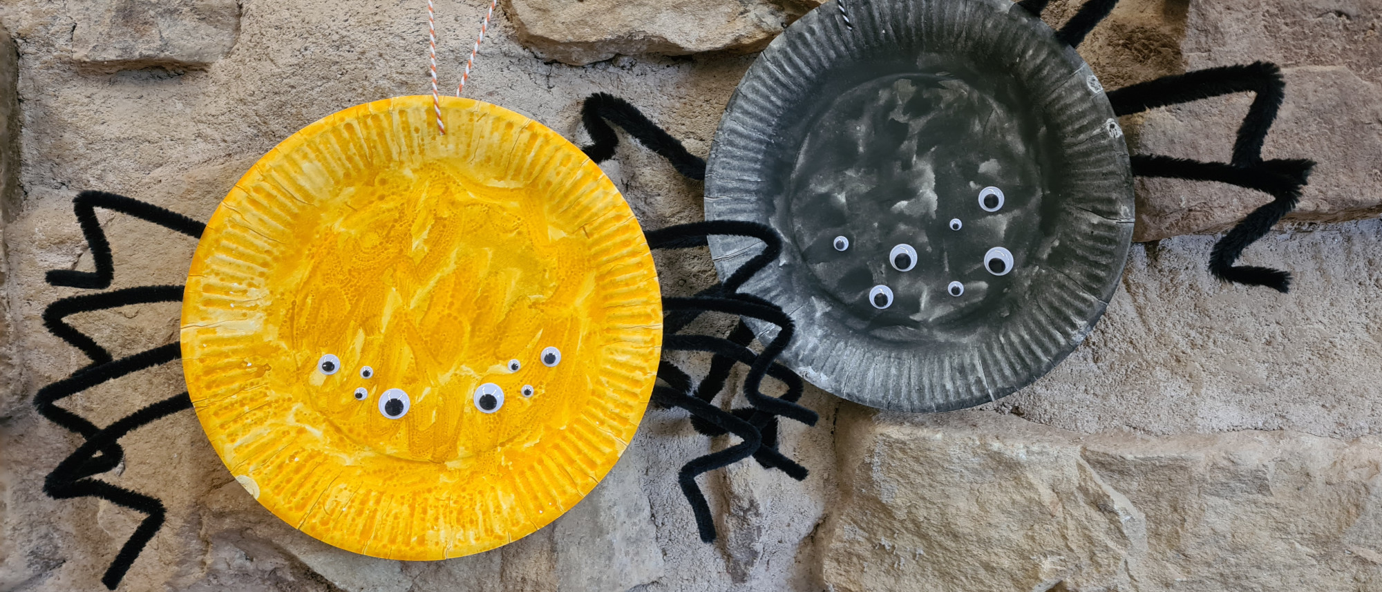 Zwei Spinnen aus Papptellern hängen an einer Steinwand