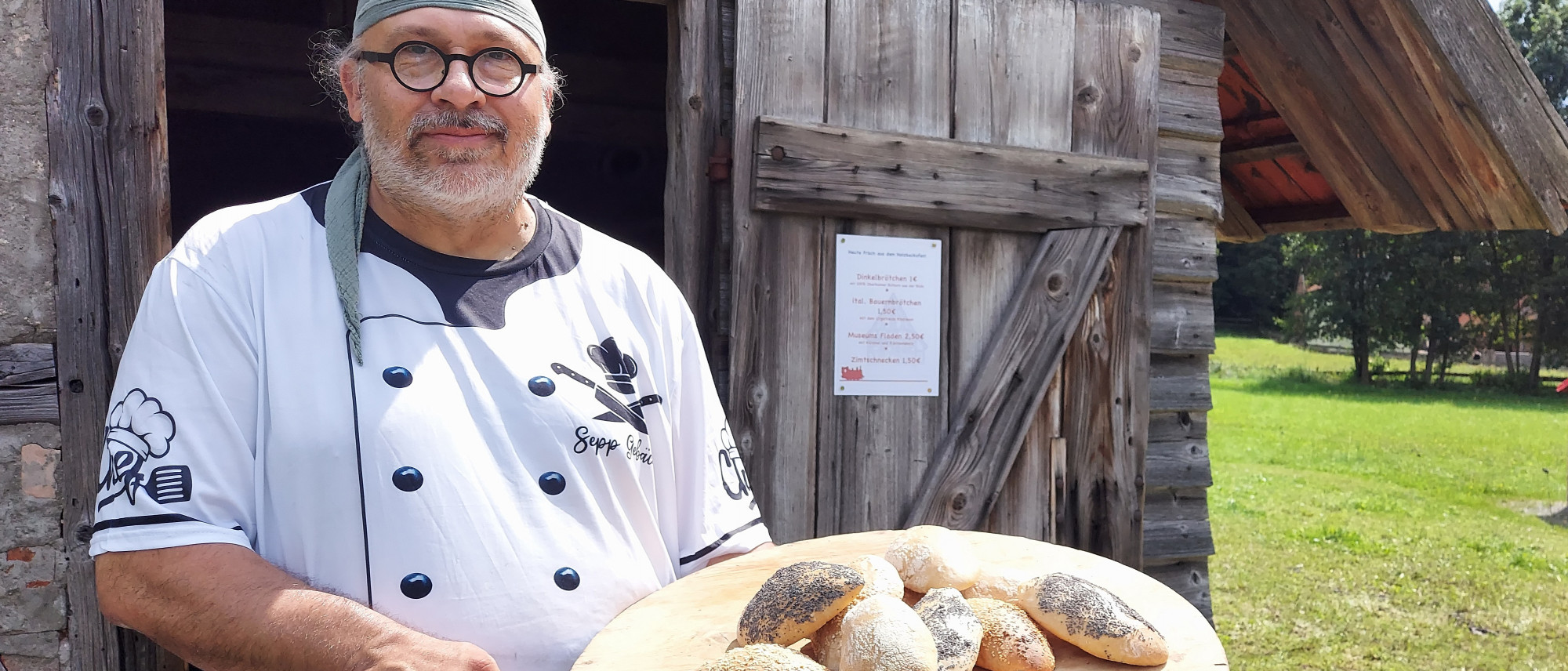 Mann steht mit Brötchen auf Brett vor Backhaus