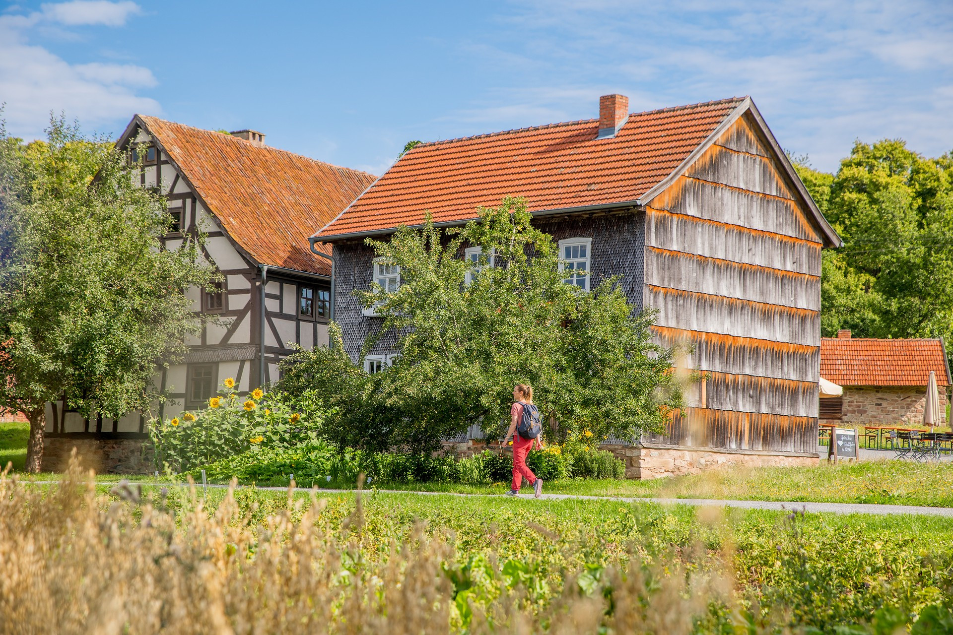 Frau spaziert durchs Freilandmuseum Fladungen, im Vordergrund Felder, im Hintergrund historische Häuser