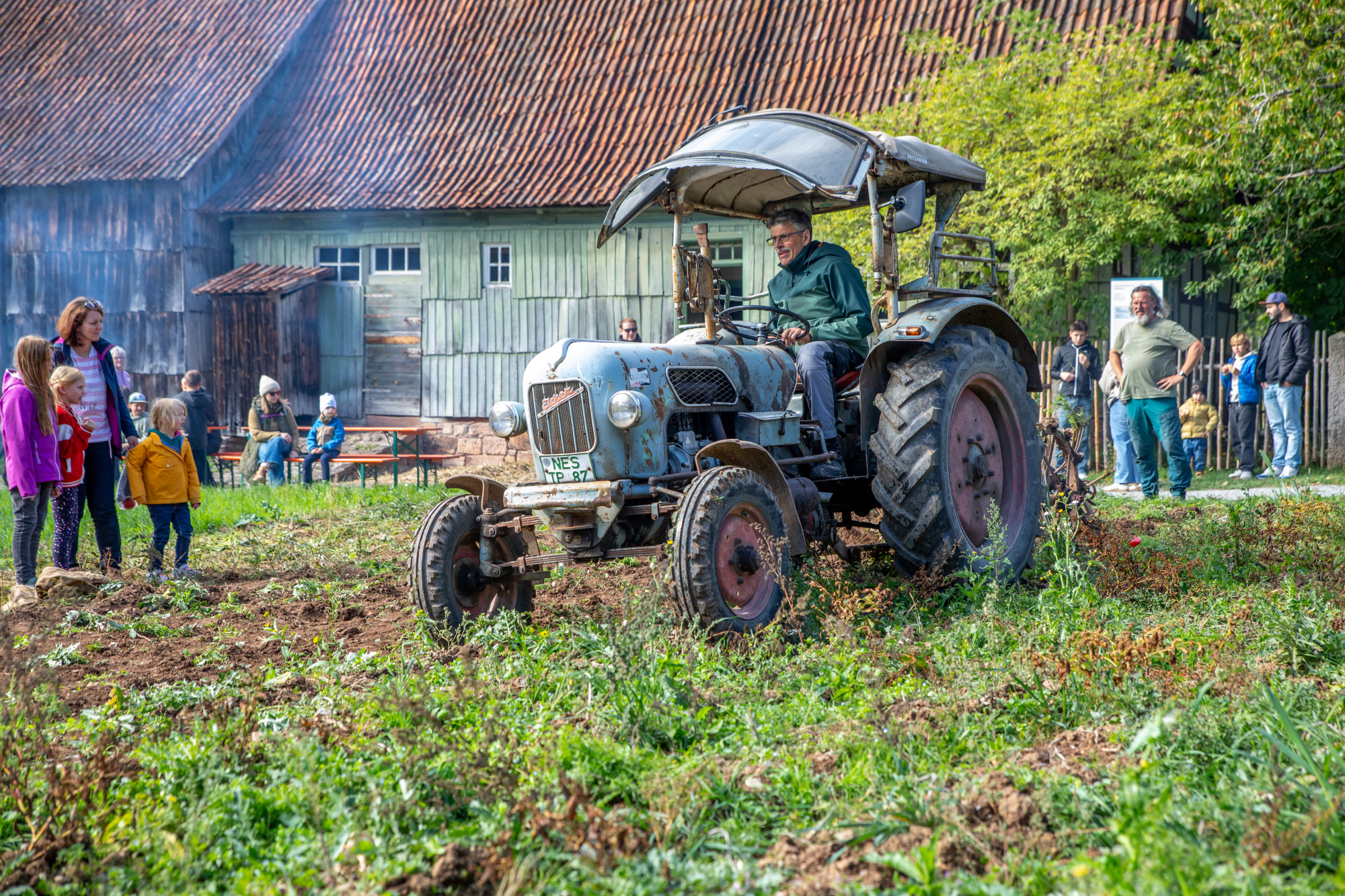 Mann bef&auml;hrt ein Feld auf einem Traktor, Personen stehen drumherum