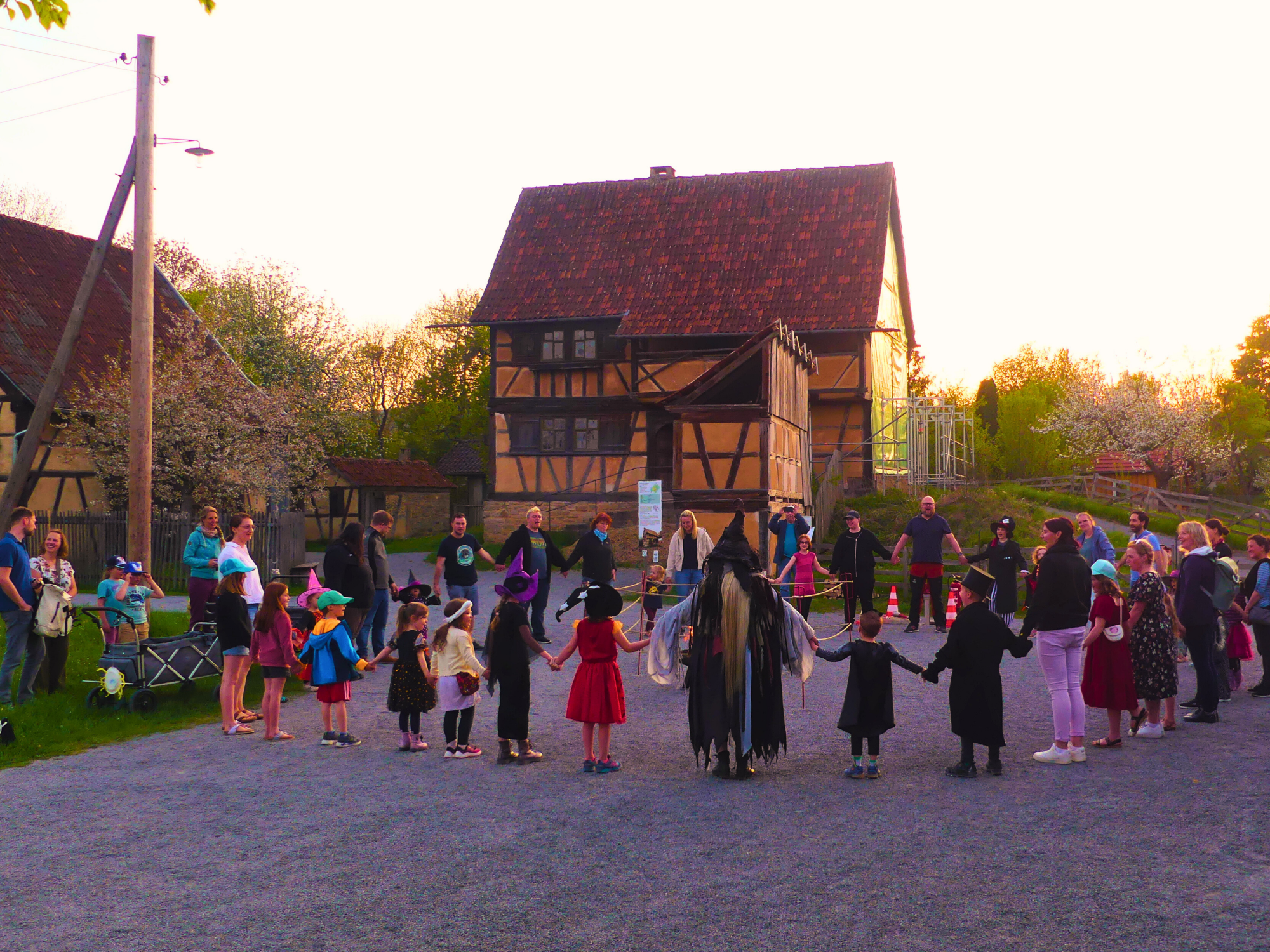 Kinder und Erwachsene stehen vor Fachwerkgeb&auml;ude im Kreis und halten sich an den H&auml;nden
