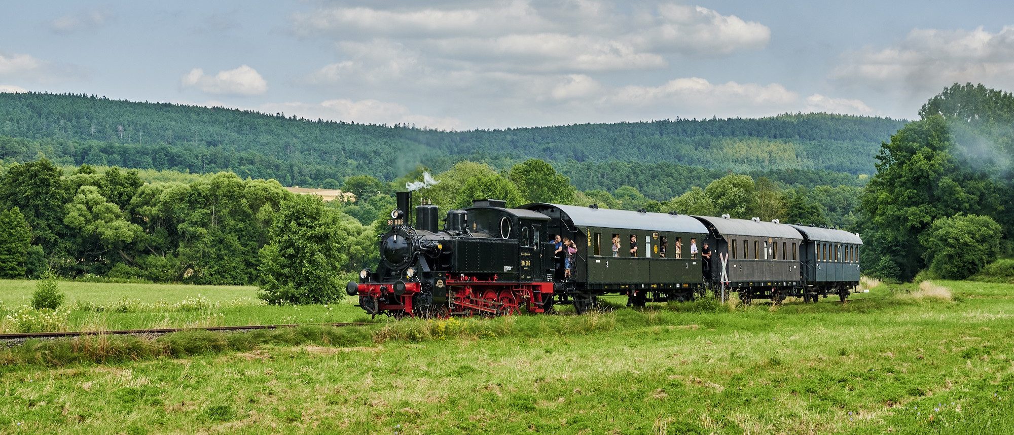 Dampfeisenbahn mir drei Waggons f&auml;hrt durch gr&uuml;ne Landschaft