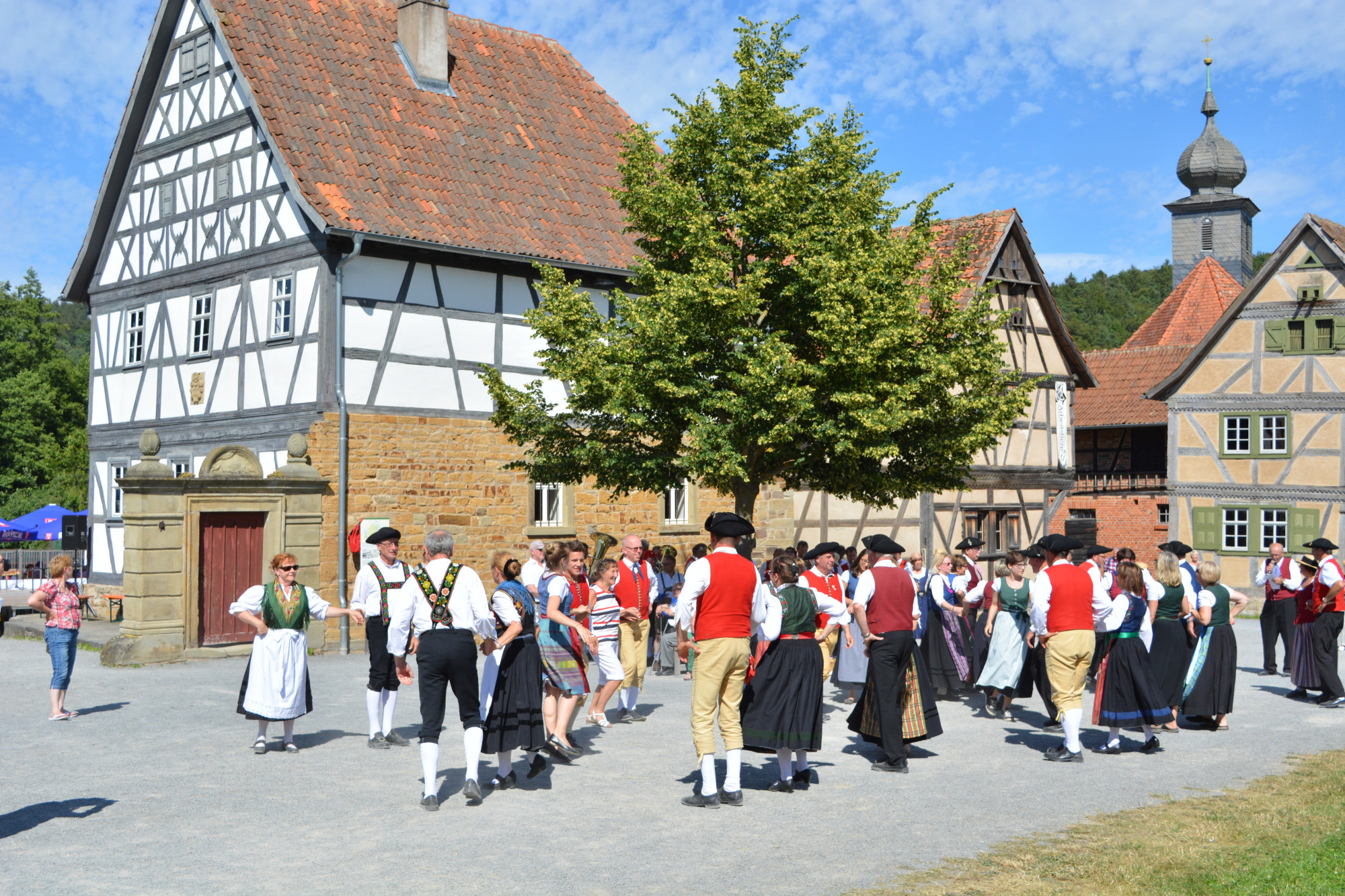 Menschen in Tracht tanzen vor Fachwerkh&auml;usern