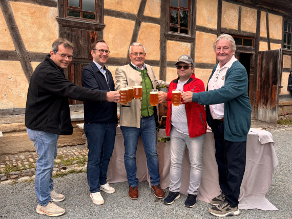 Gruppenbild mit f&uuml;nf M&auml;nnern, die sich mit Bier zuprosten