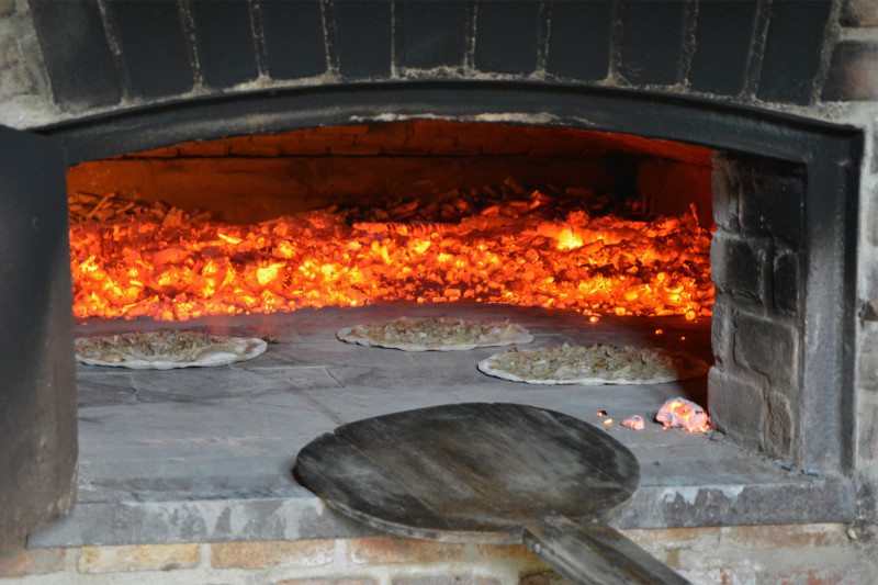 Drei R&ouml;ner Ploatze liegen in einem traditionellen Steinofen mit gl&uuml;hender Holzkohle und einem Holzschieber davor